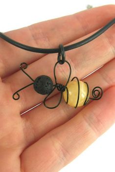 a hand holding a wire wrapped necklace with a yellow heart and black bead on it