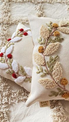 two embroidered pillows sitting on top of a white rug next to each other with red and yellow flowers