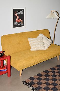 a yellow couch sitting next to a red table with a lamp on top of it