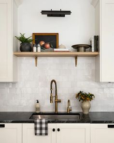 a kitchen with white cabinets and black counter tops is pictured in this image, there are two vases on the shelf above the sink