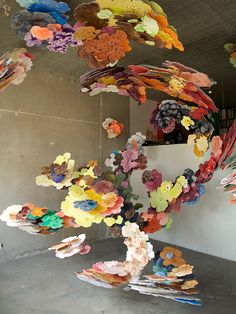 an art installation made out of paper flowers in a room with concrete flooring and walls