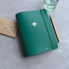 a green notebook sitting on top of a table next to a pencil and paper bag