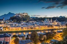 the city is lit up at night with lights shining on it and mountains in the background