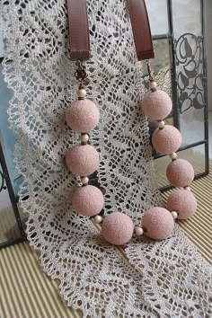 a pink necklace with wooden beads on a lace doily next to a glass case