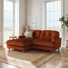 an orange couch sitting on top of a rug in a living room next to two windows