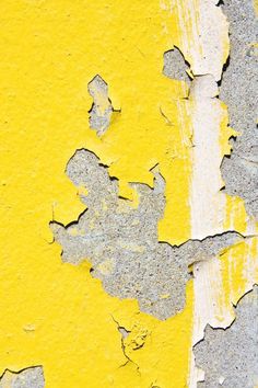 peeling paint on the side of a yellow and gray wall with white lines in it