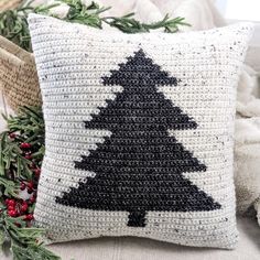 a crocheted pillow with a black and white christmas tree on it next to evergreen branches