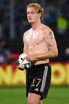 a shirtless man with no shirt standing on a soccer field holding a ball and glove