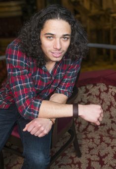 a young man sitting in a chair with his arms crossed and looking at the camera