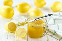 a glass jar filled with lemon curd next to sliced lemons and a spoon