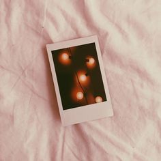 a polaroid photo with lights on it laying on a white sheeted bed spread