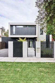 a modern house with black and white fences on the front yard, surrounded by grass