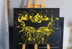 a batman painting on an easel with yellow paint splattered over the bat symbol