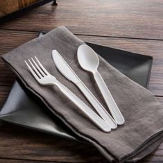 three forks and two spoons sitting on top of a black plate next to a gray napkin