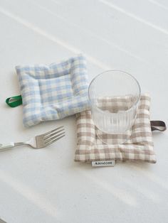 a glass, fork and napkin sitting on top of a white table with a blue checkered cloth