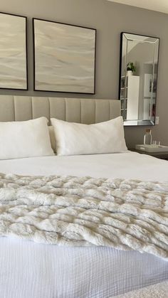 a bed with white sheets and pillows in a bedroom next to two framed pictures on the wall