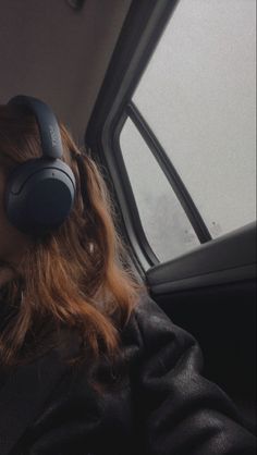 a woman with headphones on sitting in a car looking out the window at something