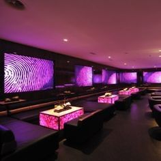 a room filled with lots of couches and tables covered in purple lighting next to wall mounted screens