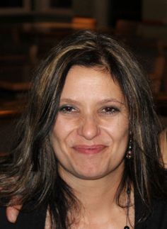 a woman smiling for the camera with her hair blowing in the wind and wearing a black top