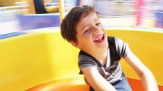 a young boy riding on top of a yellow and orange playground ride at a park