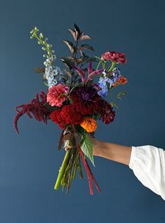 a person holding a bouquet of flowers in their hand, against a blue sky background