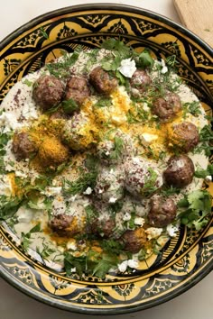 a yellow and black bowl filled with meatballs covered in cheese, herbs and seasoning