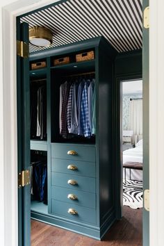 an open closet with drawers and clothes hanging on the doors, in front of a bed