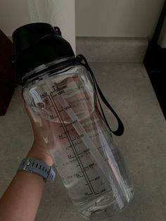 a hand holding a blender bottle with measuring tape on the bottom and strap around it