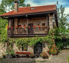 an old stone house with red flowers on the balconies and brick roofing