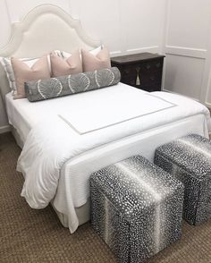 a white bed with pillows and two stools in front of it on the carpeted floor