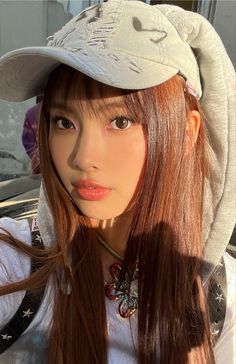 a girl with long hair wearing a hat and looking at the camera while standing in front of a car