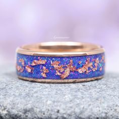 a wedding band with pink and blue glitter inlaying the center, on top of a rock