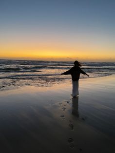 a woman standing on top of a sandy beach next to the ocean at sunset with her arms outstretched