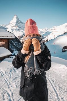 a woman standing on top of a snow covered slope holding her hands up to her face