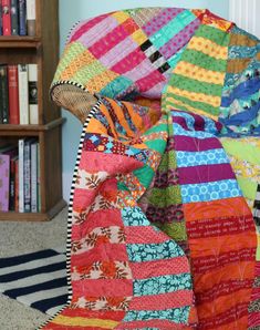 a multicolored quilt on the floor in front of a book shelf and bookshelf