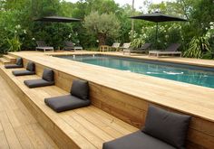 a wooden deck with lounge chairs and an above ground swimming pool surrounded by greenery