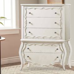 a white dresser sitting next to a window in a room with a rug on the floor