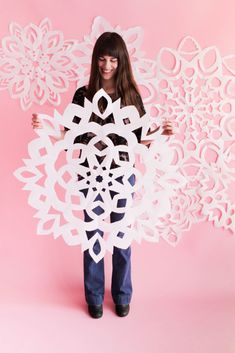 a woman holding up a cut out snowflake in front of her face on a pink background