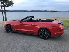 a red convertible car parked in front of a lake