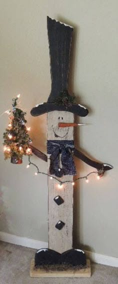 a wooden snowman with a top hat, scarf and bow tie holding a christmas tree