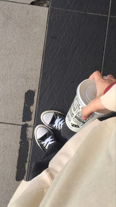 a person with their feet on the ground holding a coffee cup and wearing tennis shoes