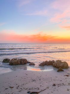 the sun is setting over the ocean with rocks in the foreground and water on the other side