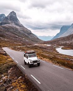 a white truck driving down a road in the middle of mountains with water and grass