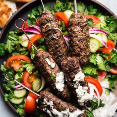 a plate filled with meat and veggies on skewers next to pita bread