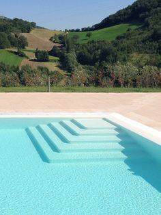 an empty swimming pool with steps leading up to the water and hills in the background