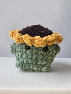 a small crocheted pot holder with a hat on it's head, sitting on a white surface