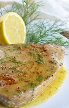 a piece of meat on a white plate with lemon and dill garnish