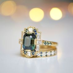 an emerald colored ring with white and blue diamonds on it's sides, sitting on a table