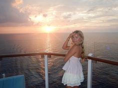 a beautiful young woman standing on the deck of a cruise ship at sunset, looking off into the distance