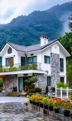 a white house with flowers in front of it and mountains in the backround